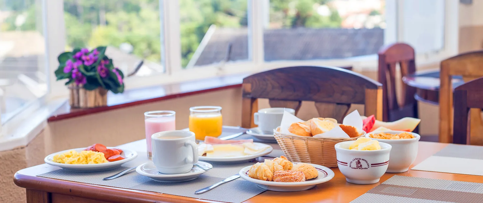 Mesa de café da manhã com pães, ovos e suco, com vista para a serra